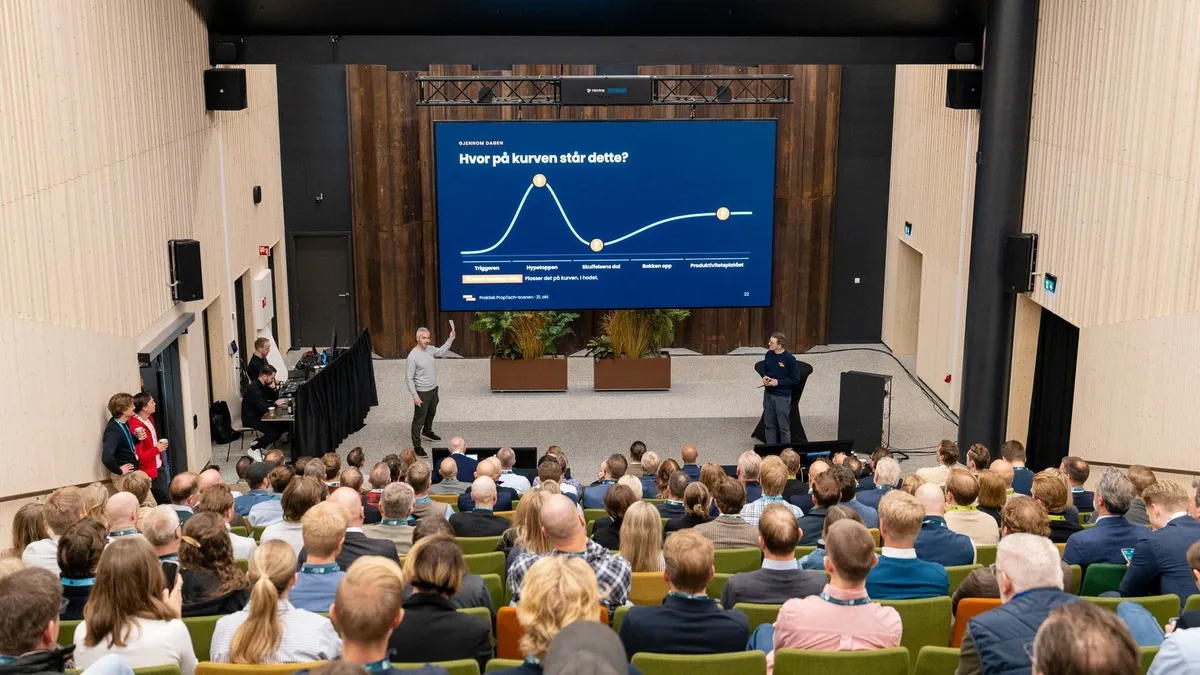 Praktisk PropTech-scenen sett fra bakerst i salen: Tommy og Martin på scenen foran storskjermen med hype-kurven og spørsmålet «Hvor på kurven står dette?»