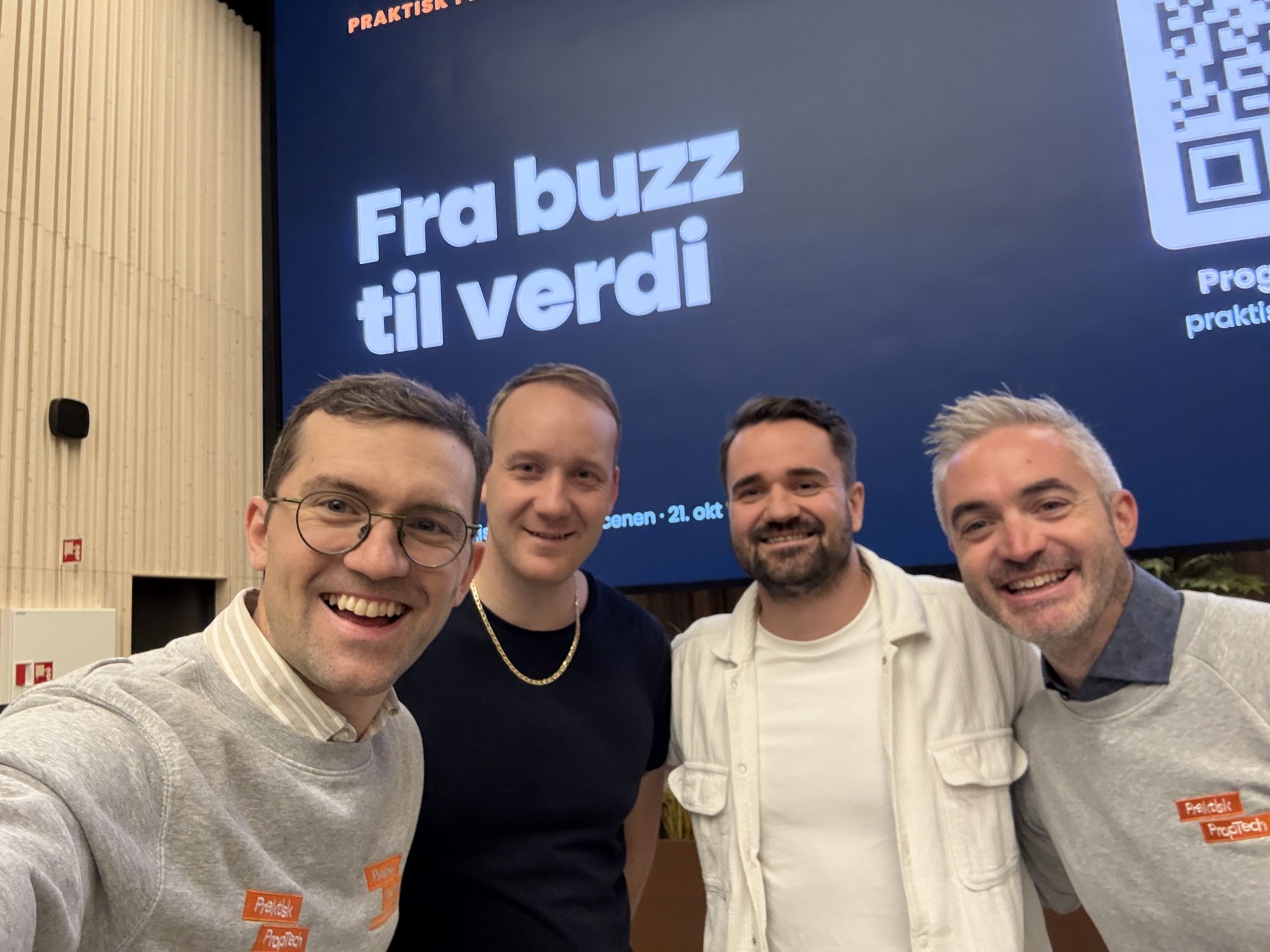 Martin og Tommy i Praktisk PropTech-gensere sammen med Torgeir og Hans Robert foran storskjermen med «Fra buzz til verdi»